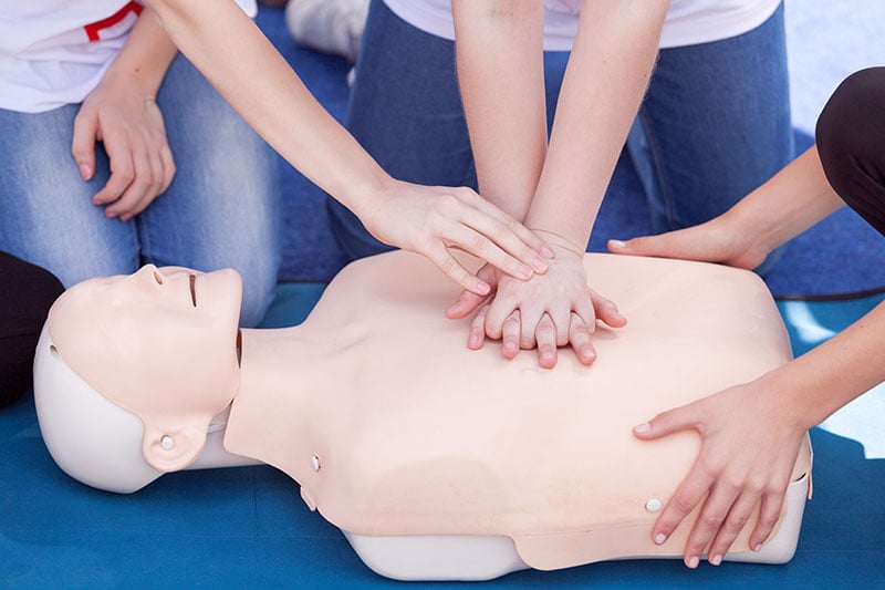 First aid instructor demonstrating CPR chest compressions on training mannequin during certification course