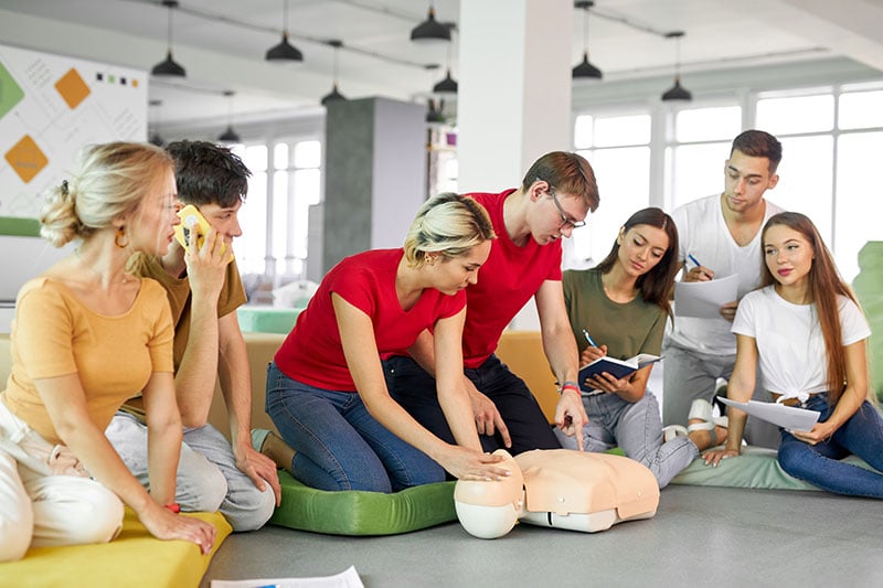 First Aid instructor demonstrating CPR technique on training manikin during hands-on course